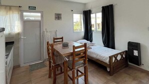 A small, clean room with a bed, a table with chairs, a ceiling fan, a window with curtains, and a door marked "SALIDA DE EMERGENCIA". - El Remanso (San José)