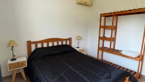 A bedroom with a wooden bed, a nightstand with a lamp, a ceiling fan, and a wooden shelf unit. - El Remanso (San José)