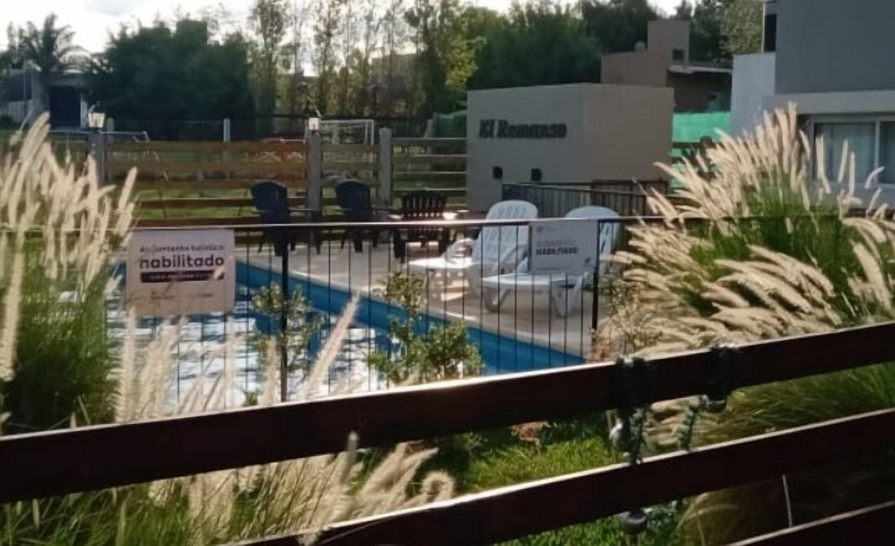 Un espace extérieur clôturé comprenant une piscine, des sièges et un panneau indiquant que l’endroit est disponible à la location.