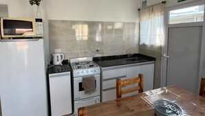A compact kitchen with a refrigerator, microwave, stove, and sink. There's a small dining table with chairs and a decorative bowl. - El Remanso (San José)