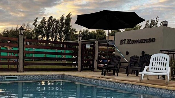 A swimming pool with lounge chairs and a covered area, surrounded by a fence and trees. - El Remanso (San José)