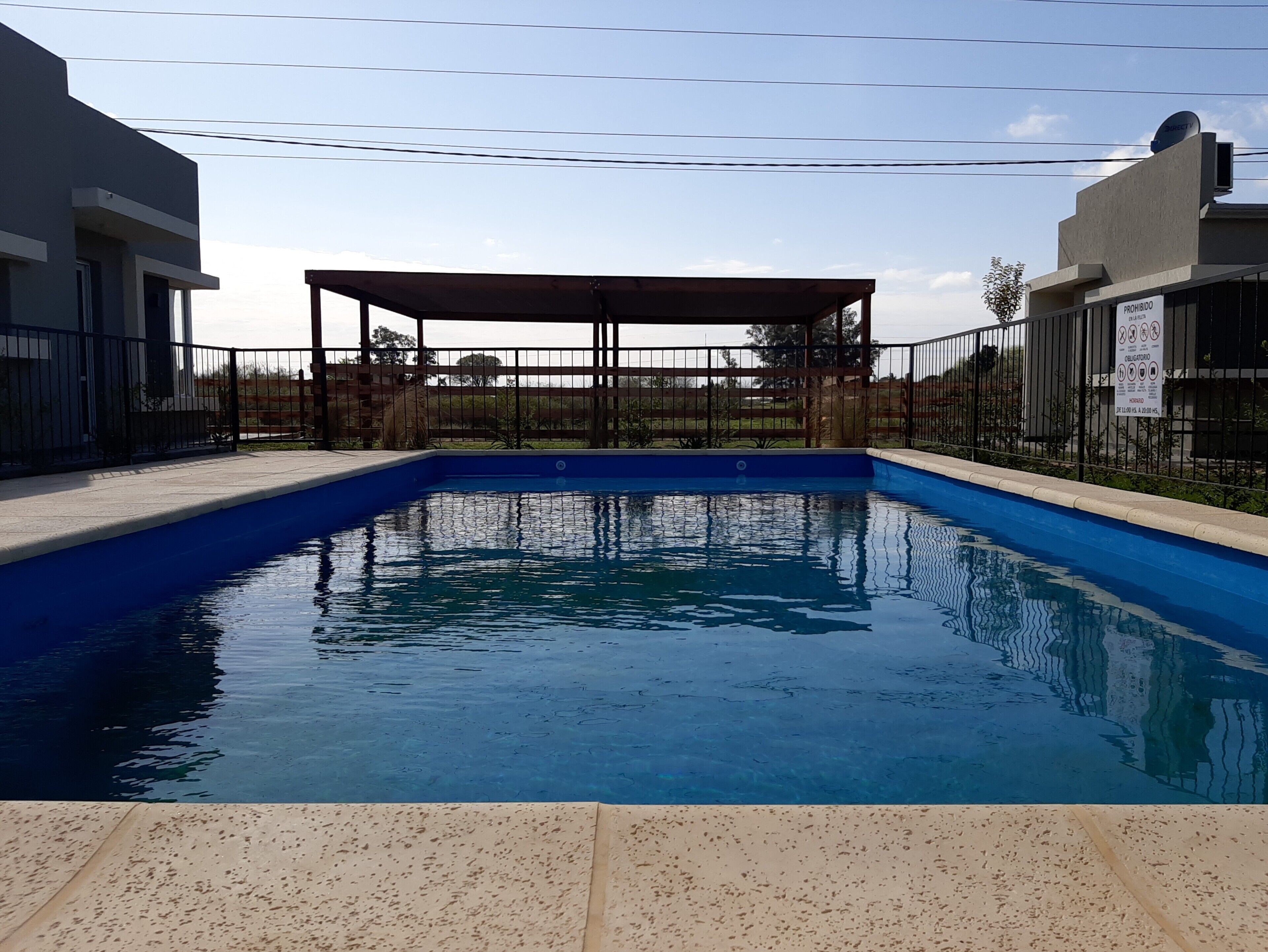 Une piscine dotée d’une zone couverte, entourée d’une clôture et d’un bâtiment.