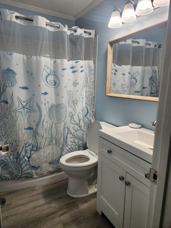 Une salle de bain équipée d’un rideau de douche orné de motifs représentant la vie marine, de toilettes, d’un lavabo et d’un miroir.