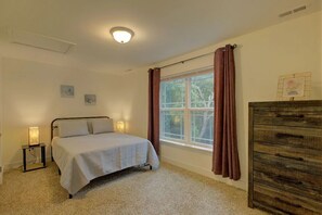 Un dormitorio con una cama, una mesita de noche con lámpara, un aparador y una ventana con cortinas.