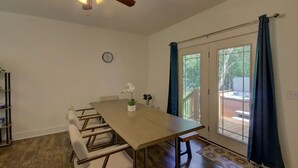 A dining area with a long table, chairs, a ceiling fan, and a view through a glass door.