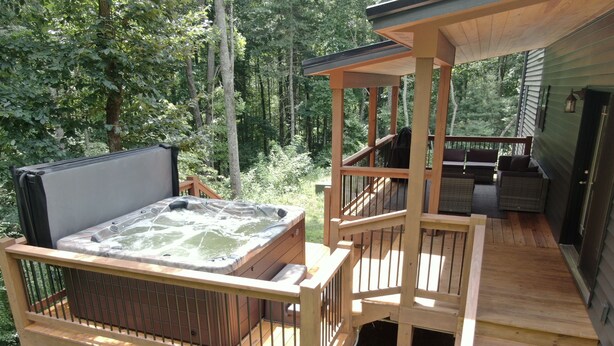 A wooden deck with a hot tub, outdoor furniture, and a covered area.