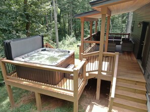 Eine Holzterrasse mit Whirlpool, Gartenmöbeln und einem überdachten Bereich.
