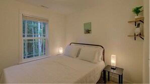 A bedroom with a bed, bedside lamps, a window, a wall-mounted shelf with a plant, and a ceiling light.