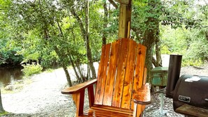 Una silla de madera sobre una cubierta de madera, con una parrilla y un letrero al fondo.