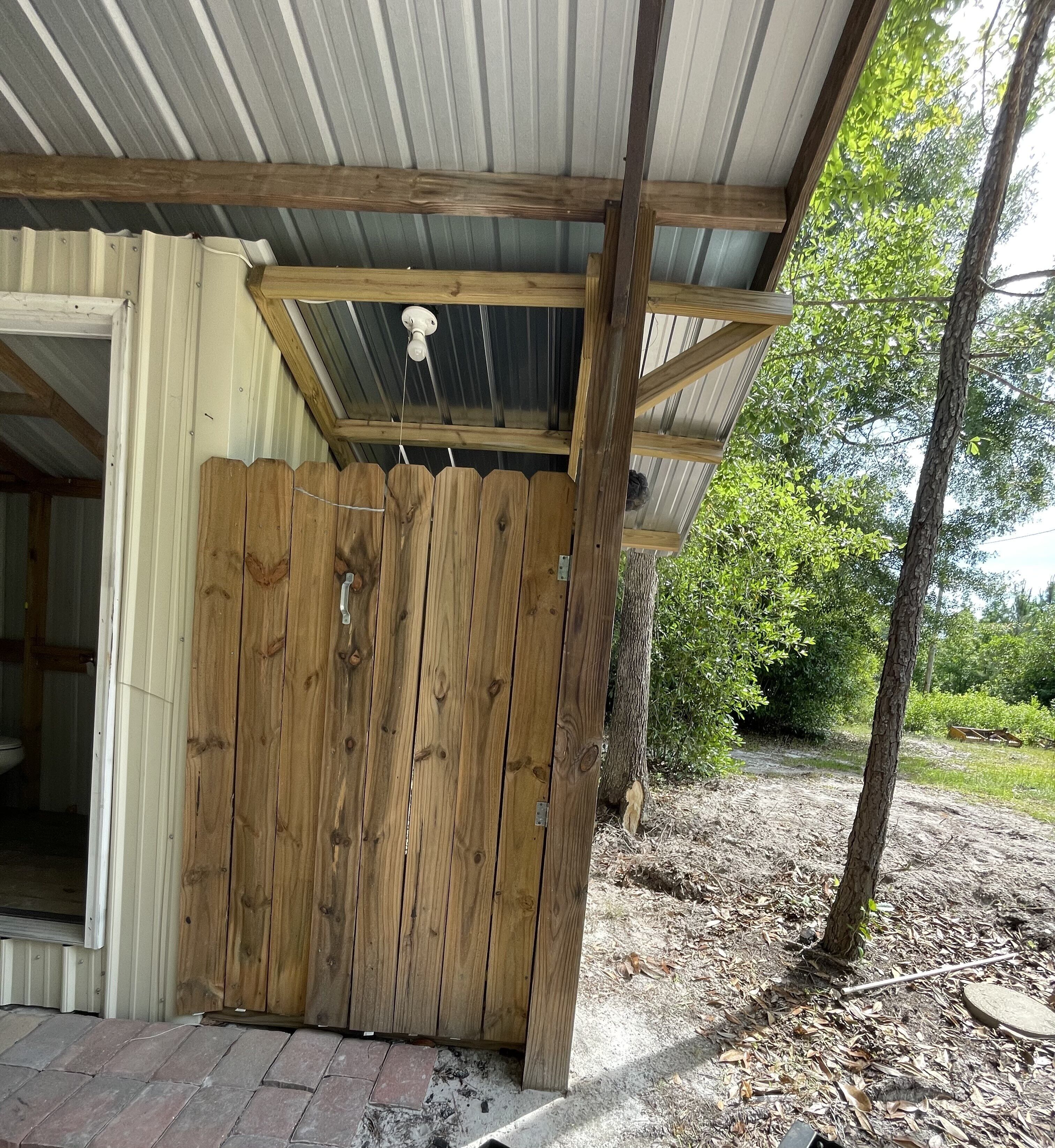 A wooden fence with a metal roof structure, a visible light fixture, and a brick pathway leading to a building.