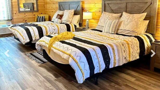 Una habitación estilo cabaña de madera con dos camas, cada una con ropa de cama estampada y cabeceros.