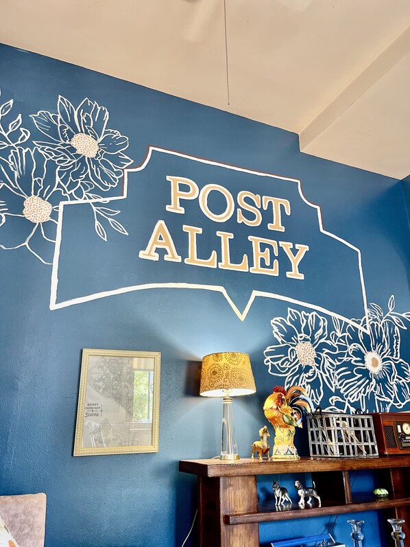 Una pared con un letrero que dice 'POST ALLEY', un mapa enmarcado, una lámpara y objetos decorativos en una estantería.