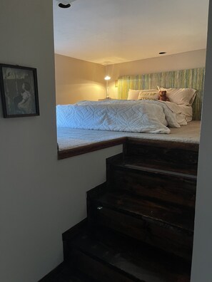 Un dormitorio con cama, un osito de peluche y una escalera que sube a otro nivel.