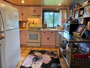 Una cocina con refrigerador, estufa, horno y un ventanal con cortinas.