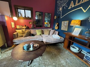 A cozy living room with a sectional sofa, a coffee table, and a wall with decorative elements including a guitar and framed artwork.