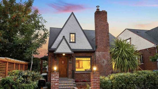 Una casa con una chimenea de ladrillo, una puerta principal de madera y una ventana pequeña sobre la puerta.