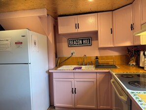 Una cocina con armarios rosados, un refrigerador blanco, un lavamanos con grifo y una estufa.