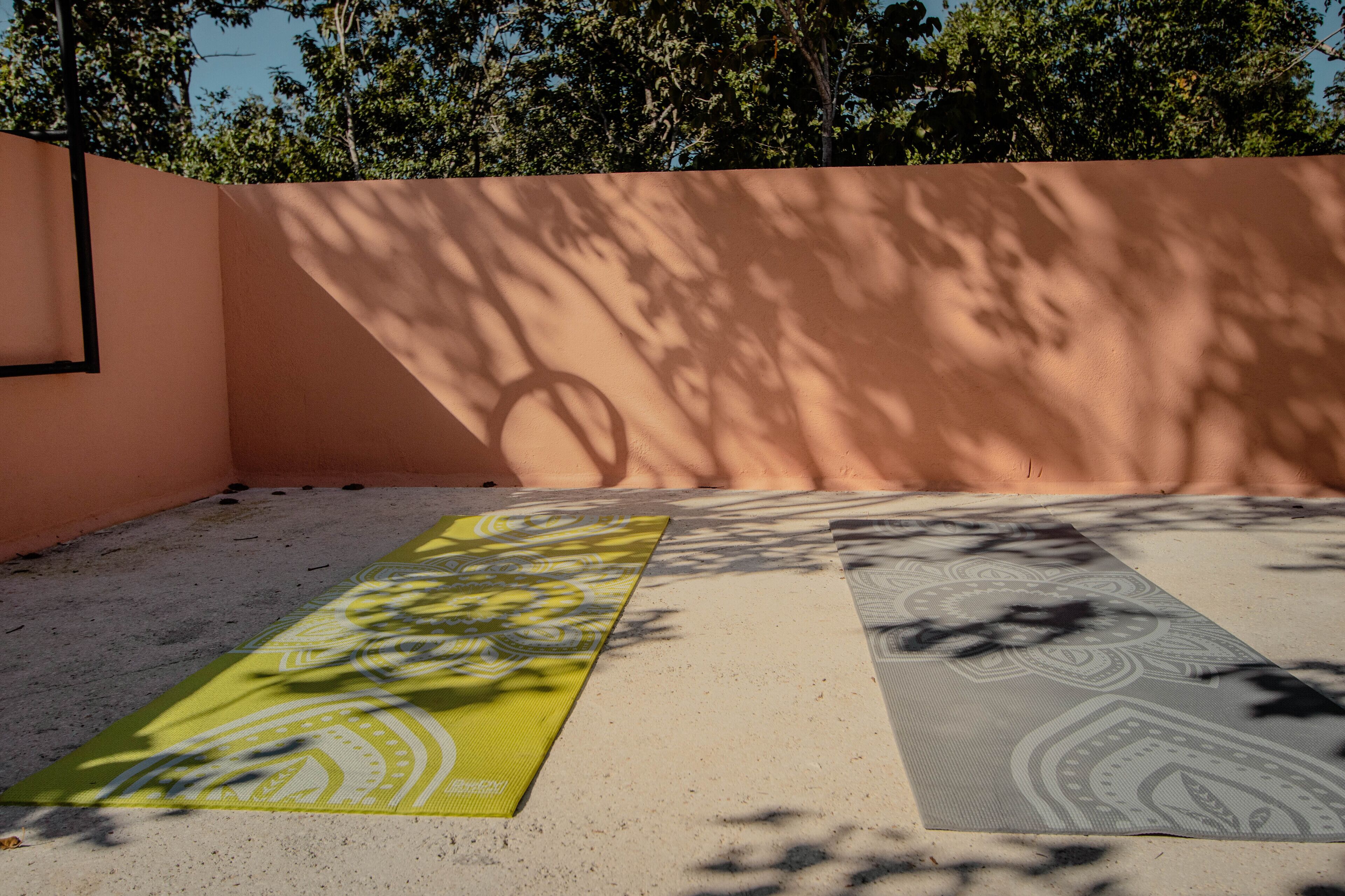 An outdoor area with a concrete floor, two yoga mats, and a wall with shadows cast by trees.