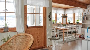 A cozy room with a wooden ceiling, a dining table with chairs, a wicker chair, and a refrigerator. - Gorgeous home in Kristinehamn (Kristinehamn)