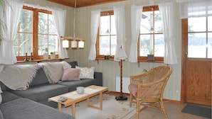 A cozy living room with a grey sofa, a wooden coffee table, and a wicker chair. There are windows with curtains, a floor lamp, and a door. - Gorgeous home in Kristinehamn (Kristinehamn)