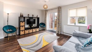 Een moderne woonkamer met een flatscreen televisie, twee blauwgroene fauteuils, een grijze bank en een tapijt met een patroon.