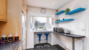 Een moderne keuken met een raam, twee blauwe barkrukken, een klok en een broodrooster.
