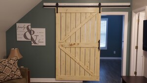 Une pièce dotée d’une porte coulissante de style grange, d’un lit agrémenté d’oreillers à motifs et d’un mur où sont accrochés deux panneaux encadrés.
