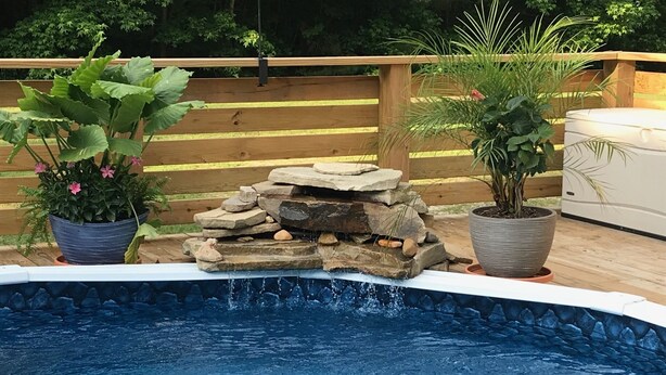 Une piscine agrémentée d’une cascade en pierre, entourée d’une terrasse en bois et de plantes en pot.