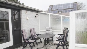 A patio with a round table and four chairs, a white brick wall, a window with frosted glass, and solar panels on a building in the background.