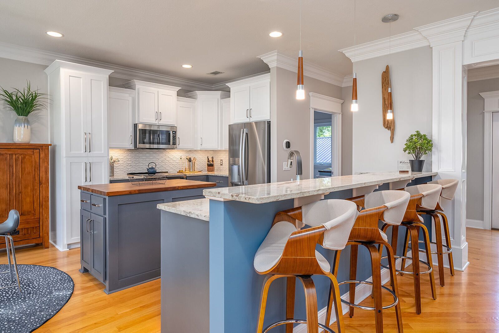 A modern kitchen with white cabinetry, stainless steel appliances, a central island with bar stools, and pendant lighting.
