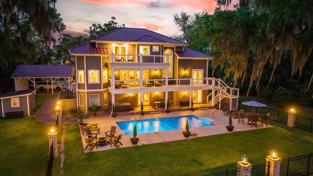 A two-story house with a swimming pool, outdoor seating, and a well-lit patio area.