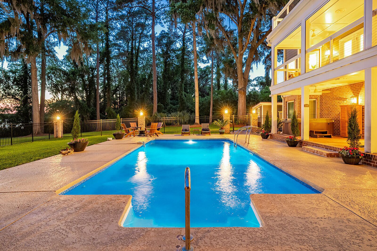Une piscine avec une zone aquatique à l’eau d’un bleu limpide, entourée d’un patio aménagé avec des sièges d’extérieur et un bâtiment bien éclairé en arrière-plan.