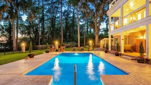 A swimming pool with a clear blue water feature, surrounded by a patio area with outdoor seating and a well-lit building in the background.
