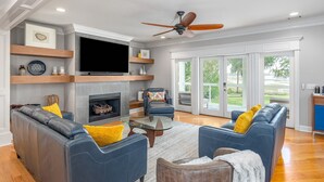 A living room with a fireplace, leather sofas, a flat-screen TV, and a ceiling fan.