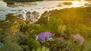 A large house surrounded by dense forest and a body of water.