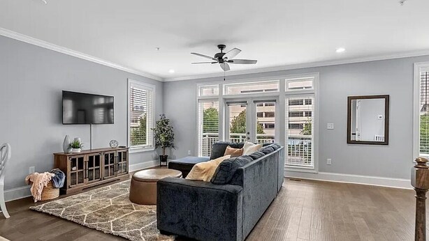 A modern living room with a dark blue sofa, a wooden cabinet, a flat-screen TV, and a ceiling fan. - Luxe 4 Story Townhouse w/Elevator, Garage (Myrtle Beach)