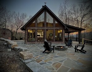 Une cabane en rondins avec un patio en pierre, un foyer extérieur et des meubles de jardin.