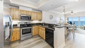 A modern kitchen with wooden cabinets, stainless steel appliances, and a large island. - Crystal Tower Unit 1508 | Snowbird Friendly | Indoor, Outdoor Pools, Hot Tub, Sauna, Gym (Gulf Shores)