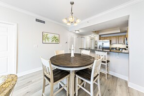 Een eetruimte met een ronde tafel en stoelen, een kroonluchter en een keuken op de achtergrond.