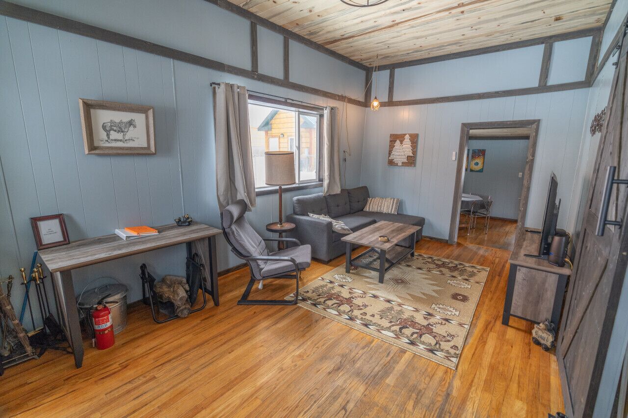 Una habitación acogedora con suelo de madera, un sofá, una mesita, una silla, un escritorio y una ventana con cortinas.