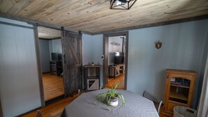 Een kamer met een houten plafond, een eettafel met een grijze tafelkleed, een kamerplant en een houten kast.