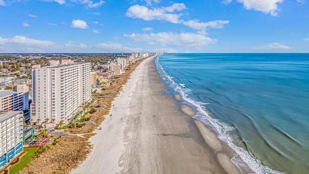 Eine Küstenstadt mit einem langen Strand, Hochhäusern und blauem Himmel.