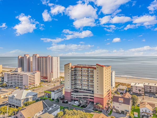A coastal hotel with multiple high-rise buildings, a parking garage, and a beach view.