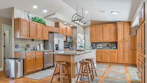 A modern kitchen with wooden cabinets, stainless steel appliances, and a central island with stools. - Rivers Edge Oasis, Our Secluded Paradise-Sleep 21+ "NEW LISTING" (Fort Myers)