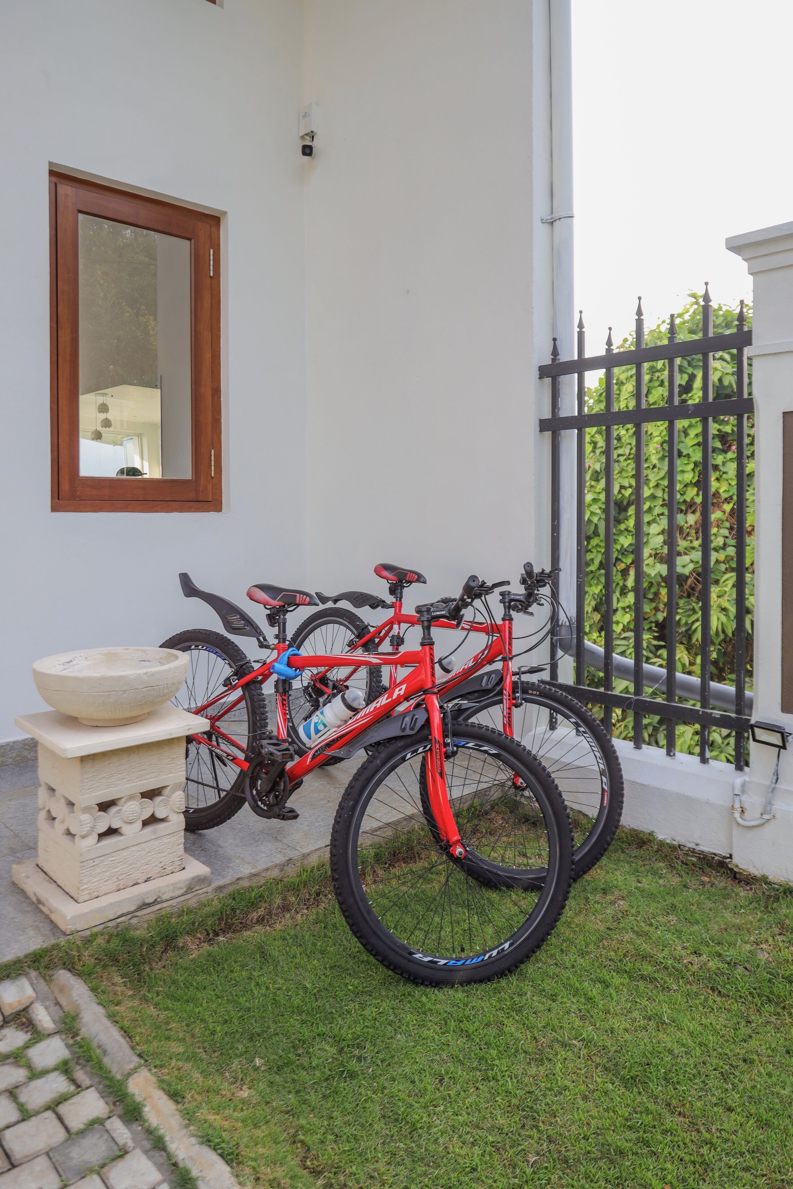 A red bicycle parked outside a building with a white exterior, a wooden-framed mirror, and a black metal gate.