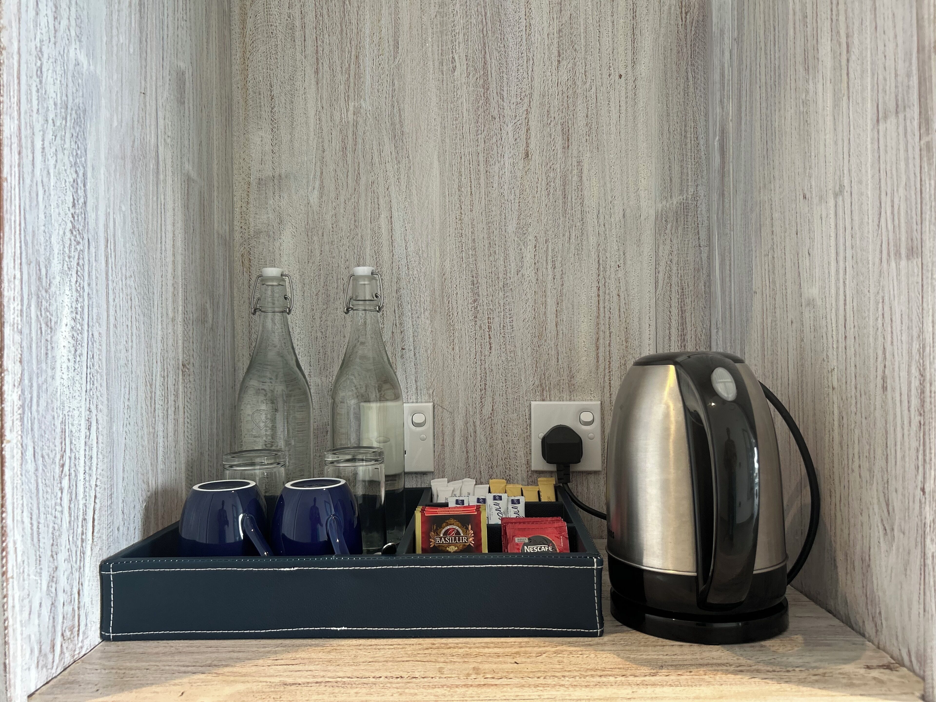 A coffee maker, two glass bottles, and a box of coffee pods on a shelf.
