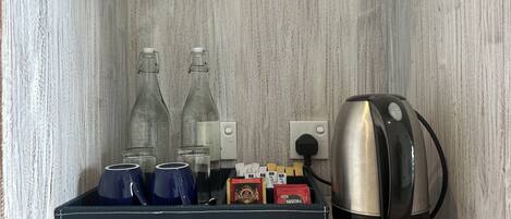 A coffee maker, two glass bottles, and a box of coffee pods on a shelf.