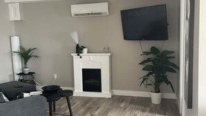 Ein Wohnzimmer mit Kamin, einem flachbildfernseher an der Wand und einem grauen Sofa.