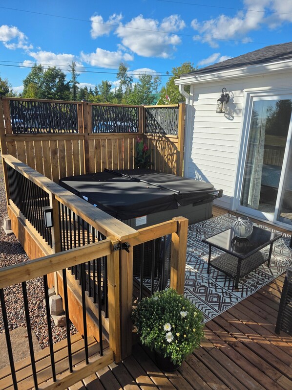 Una terraza de madera con un jacuzzi, una mesa de patio y un jarrón, y una planta en maceta.