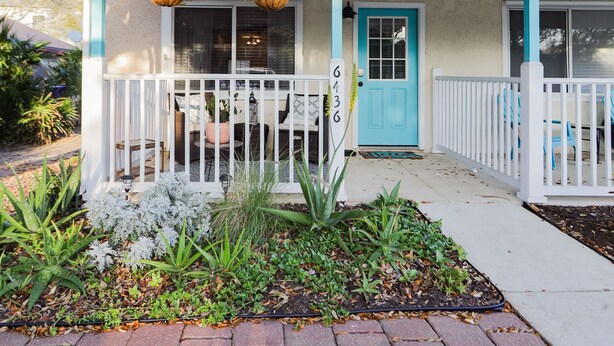 A two-story house with a blue door and white shutters, a front porch with white railings, and hanging flower baskets.
